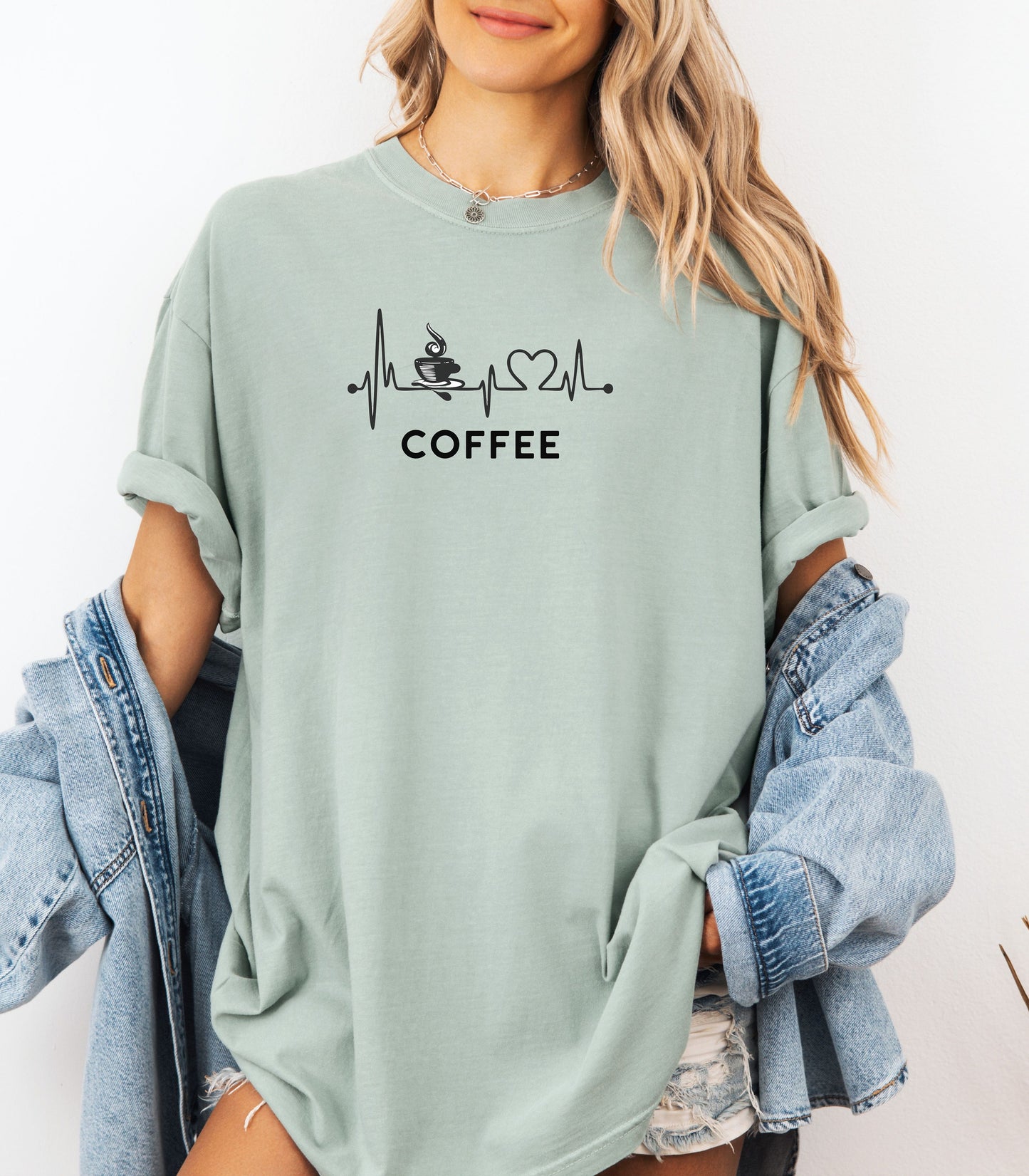 Graphic bay t-shirt design featuring a heartbeat line that flows through a steaming coffee cup and forms a heart shape before if finishes. A creative and stylish illustration that shows coffee is essential to life—perfect for caffeine lovers, baristas, and anyone whose heart beats for coffee.