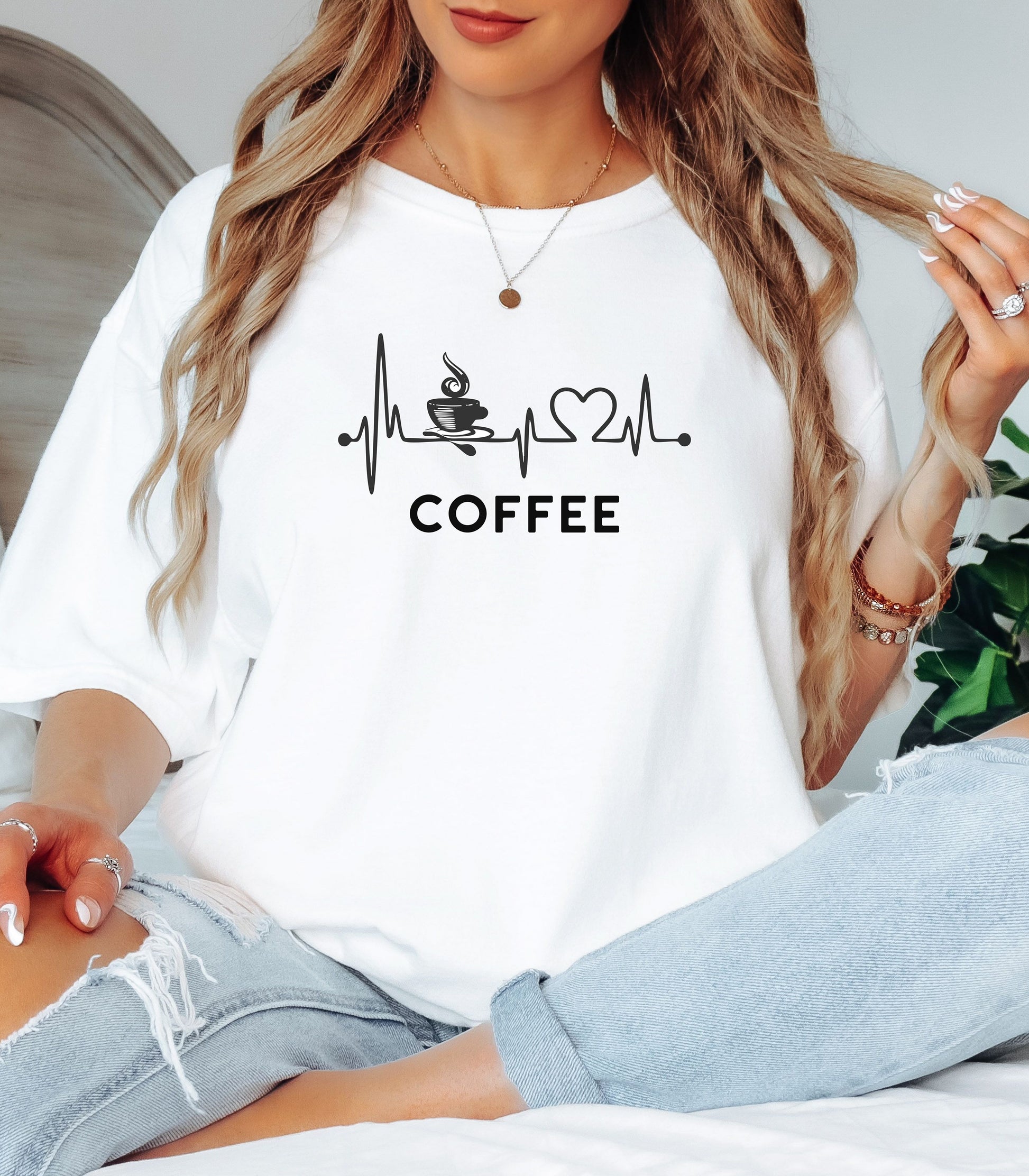 Graphic white t-shirt design featuring a heartbeat line that flows through a steaming coffee cup and forms a heart shape before it finishes. A creative and stylish illustration that shows coffee is essential to life—perfect for caffeine lovers, baristas, and anyone whose heart beats for coffee.