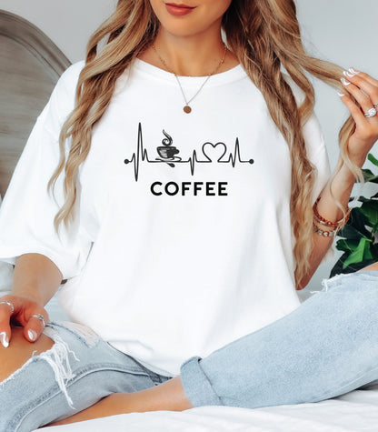 Graphic white t-shirt design featuring a heartbeat line that flows through a steaming coffee cup and forms a heart shape before it finishes. A creative and stylish illustration that shows coffee is essential to life—perfect for caffeine lovers, baristas, and anyone whose heart beats for coffee.