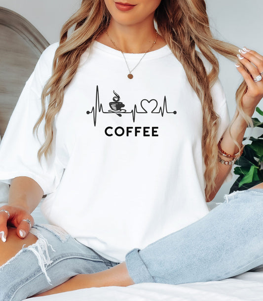 Graphic white t-shirt design featuring a heartbeat line that flows through a steaming coffee cup and forms a heart shape before it finishes. A creative and stylish illustration that shows coffee is essential to life—perfect for caffeine lovers, baristas, and anyone whose heart beats for coffee.