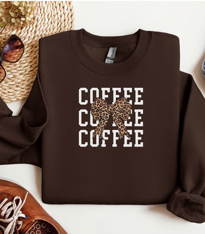 Dark Chocolate Gildan sweatshirt featuring a bold white triple “COFFEE” text stacked vertically, accented with a stylish leopard-print coquette bow at the center. A trendy and playful design that blends coffee love with fashionable flair—perfect for cozy mornings and confident, cute style.