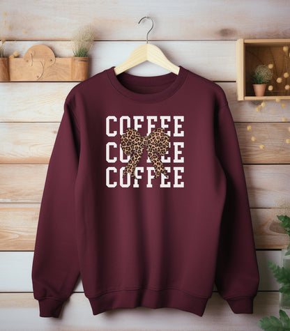 Maroon Gildan sweatshirt featuring a bold white triple “COFFEE” text stacked vertically, accented with a stylish leopard-print coquette bow at the center. A trendy and playful design that blends coffee love with fashionable flair—perfect for cozy mornings and confident, cute style.