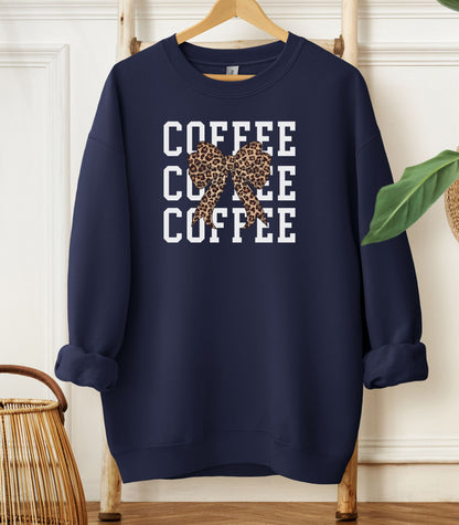 Navy Gildan sweatshirt featuring a bold white triple “COFFEE” text stacked vertically, accented with a stylish leopard-print coquette bow at the center. A trendy and playful design that blends coffee love with fashionable flair—perfect for cozy mornings and confident, cute style.