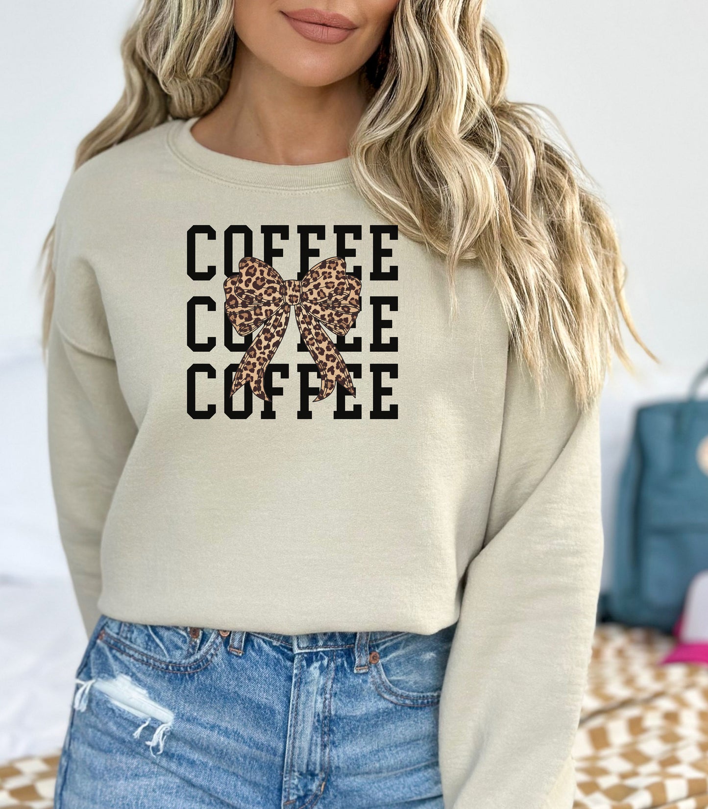 Sand Gildan sweatshirt featuring a bold black triple “COFFEE” text stacked vertically, accented with a stylish leopard-print coquette bow at the center. A trendy and playful design that blends coffee love with fashionable flair—perfect for cozy mornings and confident, cute style.