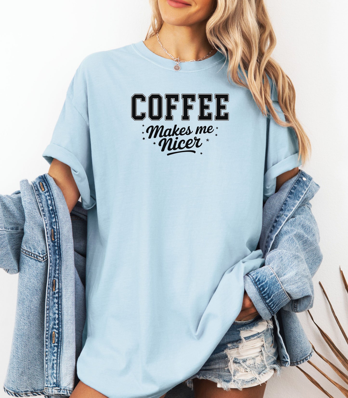 Graphic Chambray light blue t-shirt design featuring bold varsity-style black text “COFFEE” with the phrase “makes me nicer” in a playful script underneath, surrounded by small stars. A fun and relatable design perfect for coffee lovers who know their mood improves with caffeine—ideal for casual wear with a humorous twist.