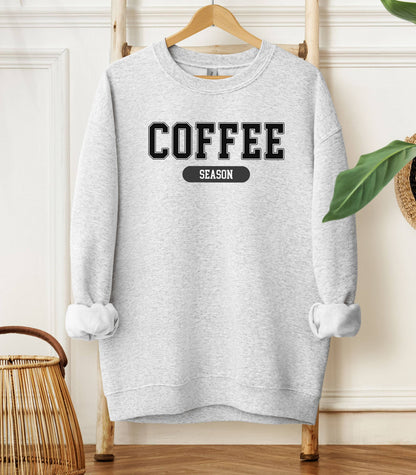 Ash sweatshirt featuring a bold “COFFEE” design in varsity-style black lettering with the word “SEASON” underneath in a rounded black label. A cozy and stylish look perfect for coffee lovers embracing their favorite time of year—whether it’s fall, winter, or every season.