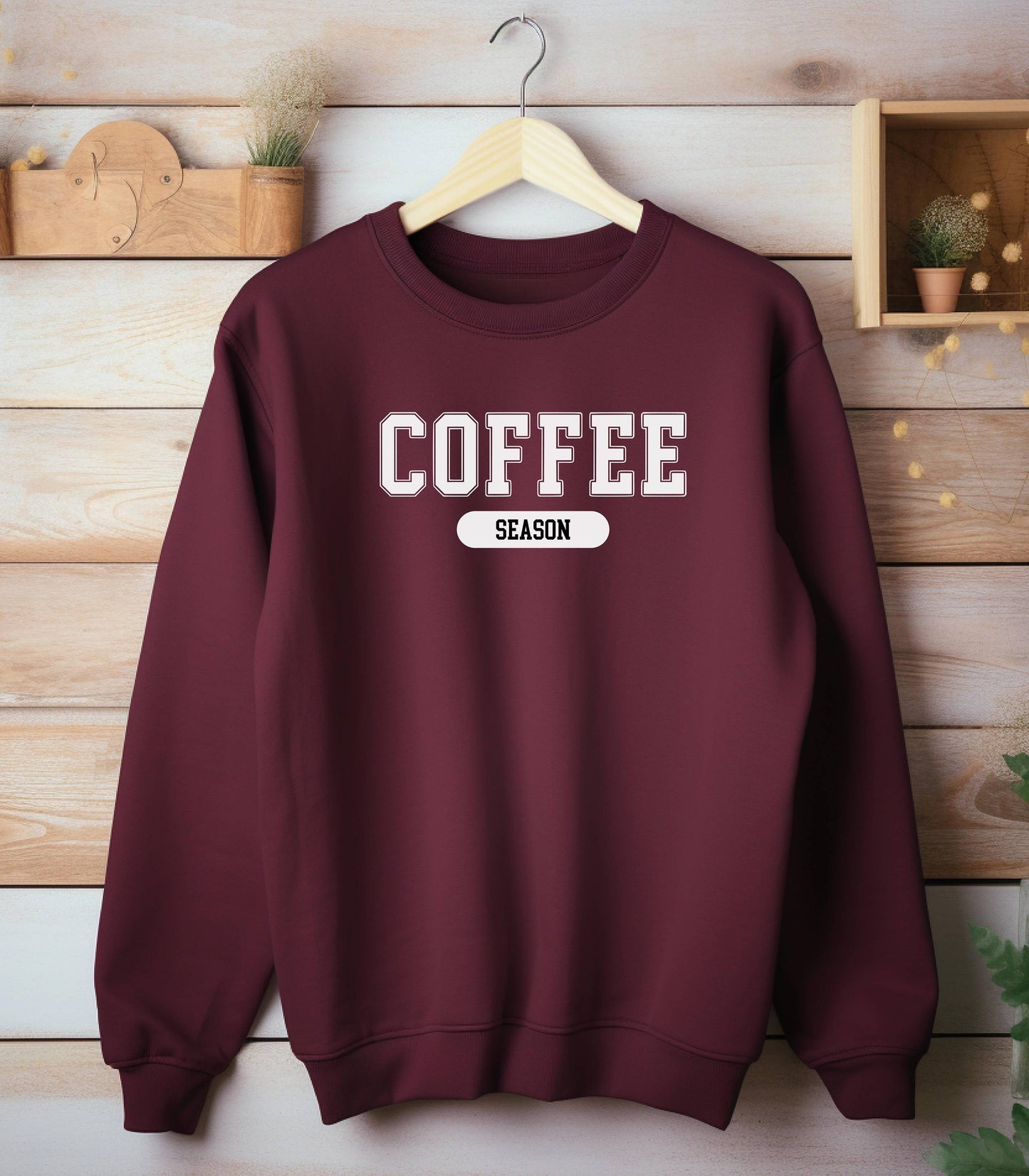 Maroon sweatshirt featuring a bold “COFFEE” design in varsity-style white lettering with the word “SEASON” underneath in a rounded black label. A cozy and stylish look perfect for coffee lovers embracing their favorite time of year—whether it’s fall, winter, or every season.
