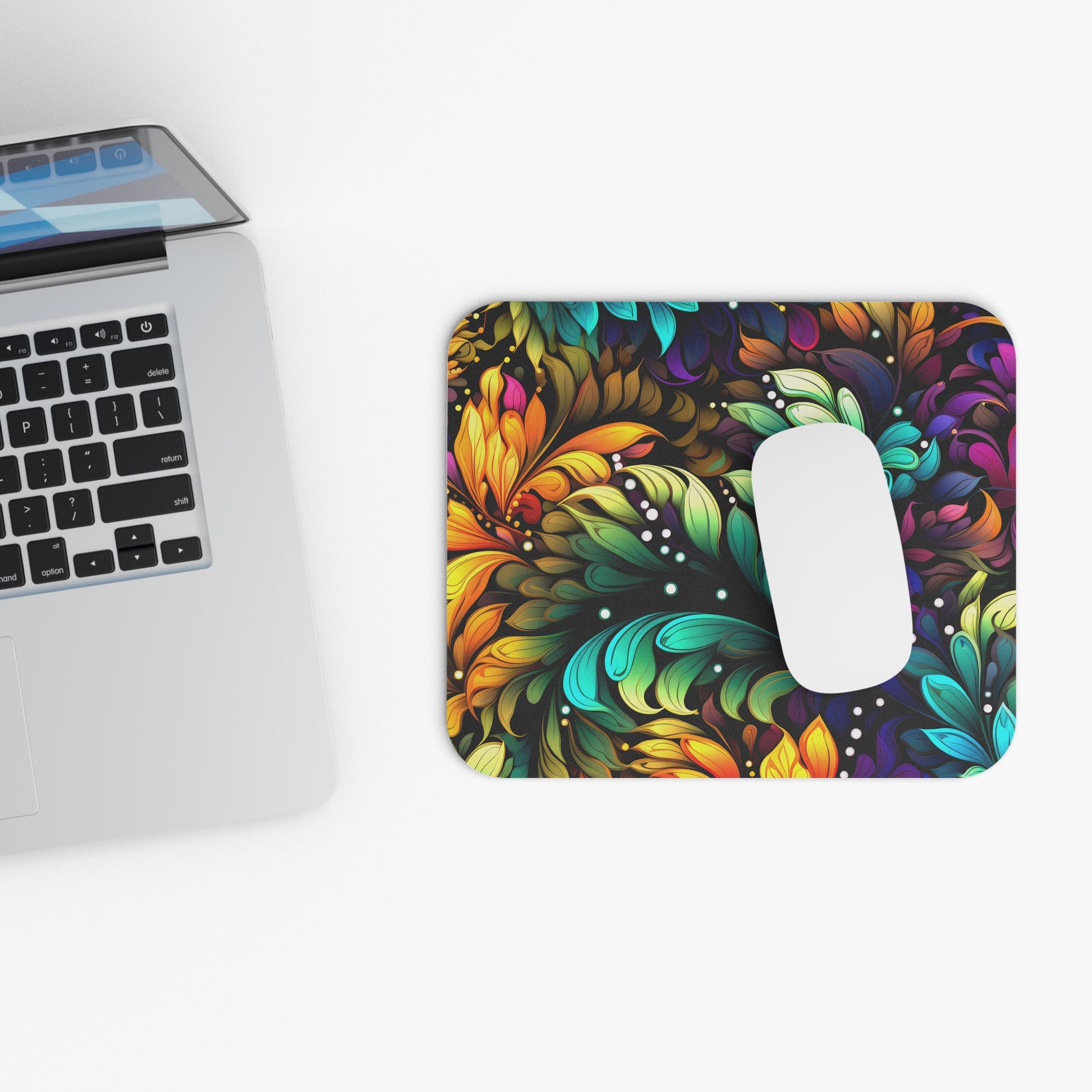 Colorful mouse pad with floral design next to a laptop on a white surface