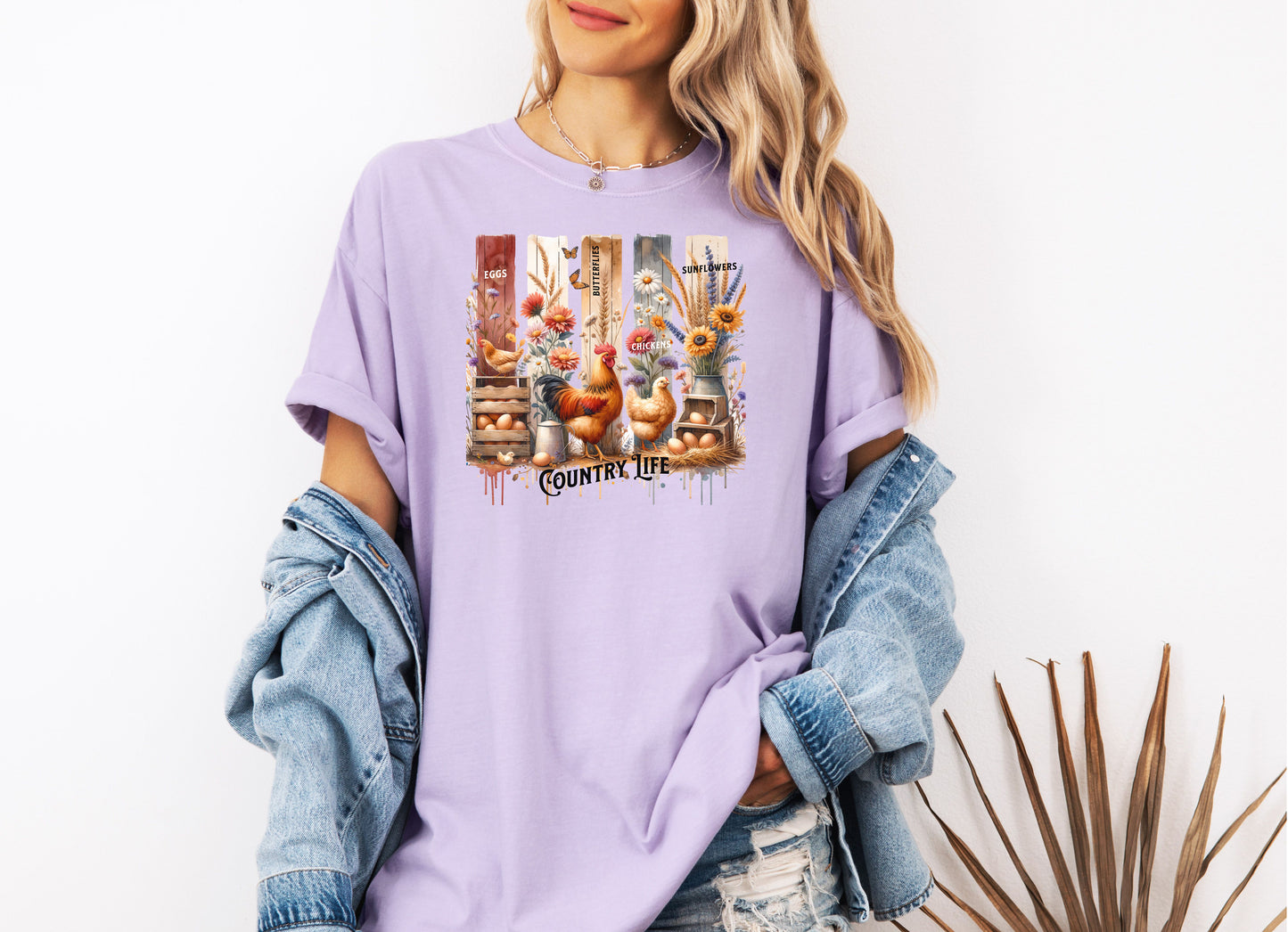 Country Life T-shirt in orchid featuring a vibrant farmhouse design with roosters, hens, eggs, sunflowers, butterflies, and rustic wooden crates. The artwork is accented with vertical watercolor panels and labeled elements like “Eggs,” “Butterflies,” “Chickens,” and “Sunflowers,” capturing the charm of rural living and barnyard beauty. Perfect for farm lovers and country style enthusiasts.