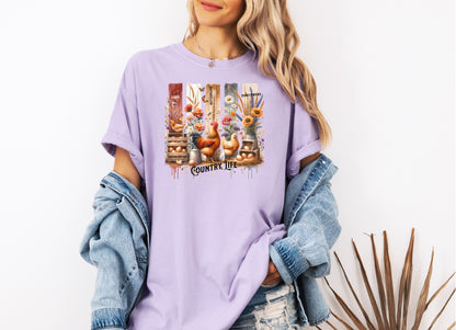 Country Life T-shirt in orchid featuring a vibrant farmhouse design with roosters, hens, eggs, sunflowers, butterflies, and rustic wooden crates. The artwork is accented with vertical watercolor panels and labeled elements like “Eggs,” “Butterflies,” “Chickens,” and “Sunflowers,” capturing the charm of rural living and barnyard beauty. Perfect for farm lovers and country style enthusiasts.