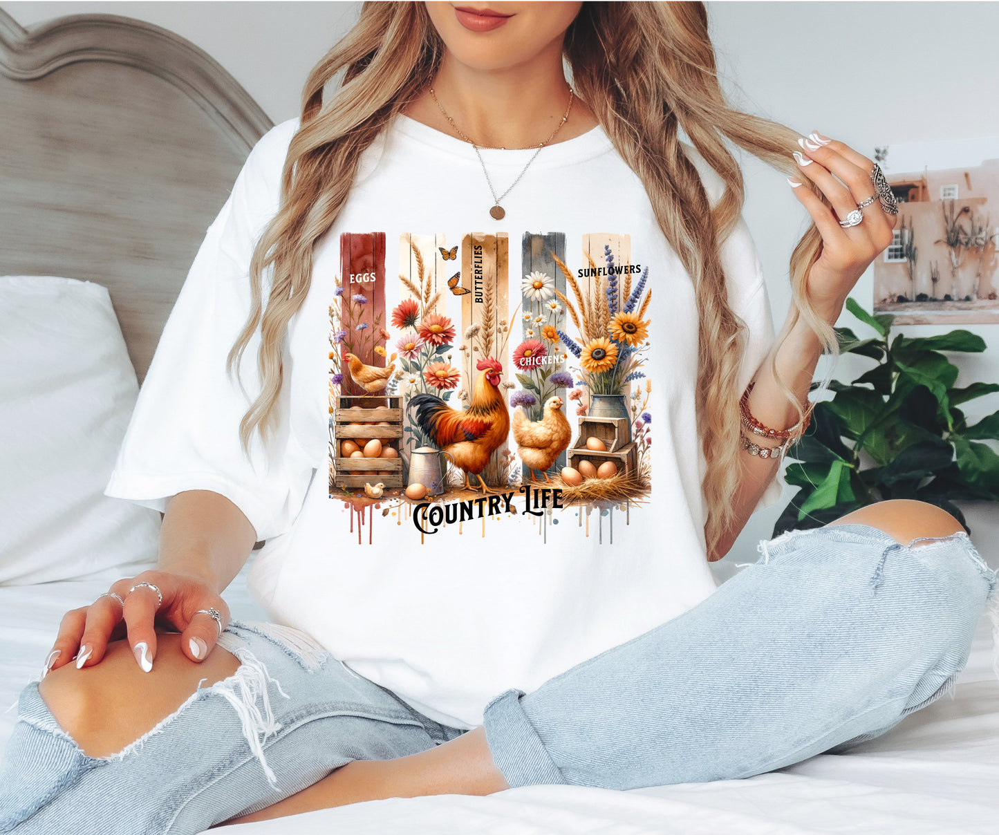 Country Life T-shirt in white featuring a vibrant farmhouse design with roosters, hens, eggs, sunflowers, butterflies, and rustic wooden crates. The artwork is accented with vertical watercolor panels and labeled elements like “Eggs,” “Butterflies,” “Chickens,” and “Sunflowers,” capturing the charm of rural living and barnyard beauty. Perfect for farm lovers and country style enthusiasts.