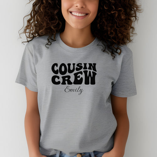 Smiling child wearing an Athletic Heather youth T-shirt with bold black "Cousin Crew" text in a playful font and personalized with “Your Name” in elegant script below. The shirt is paired with jeans, creating a fun and youthful vibe perfect for family gatherings or matching cousin outfits.