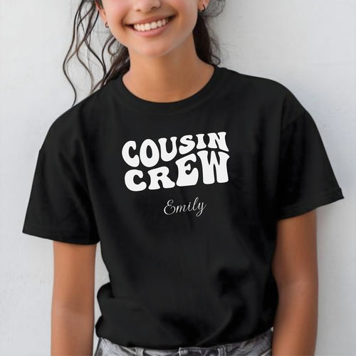 Smiling child wearing a black youth T-shirt with bold white "Cousin Crew" text in a playful font and personalized with “Your Name” in elegant script below. The shirt is paired with jeans, creating a fun and youthful vibe perfect for family gatherings or matching cousin outfits.