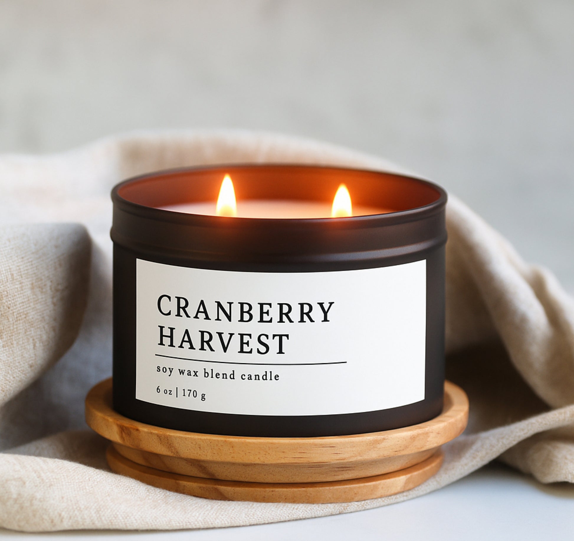 Cranberry Harvest soy wax blend candle in a black matte tin with a wooden coaster on a neutral background
