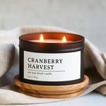 Cranberry Harvest candle in a black matte 8 oz candle tin with a wooden coaster on a neutral background