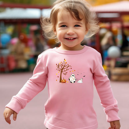 Adorable toddler wearing a pink long-sleeve T-shirt with a cute Halloween design featuring a spooky tree with falling leaves, a smiling jack-o'-lantern, and two ghost figures—one child ghost and one ghost dog. A playful and heartwarming fall design perfect for Halloween festivities and toddler apparel.