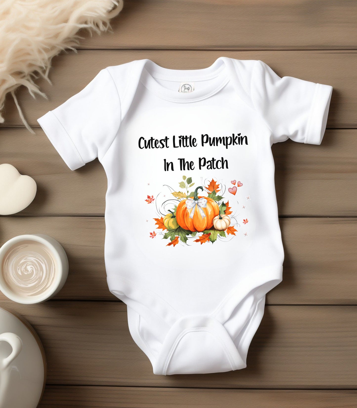 White infant bodysuit featuring the phrase "Cutest Little Pumpkin In The Patch" with an adorable fall-themed design of orange and white pumpkins, autumn leaves, hearts, and a sweet bow. Perfect for baby's first fall or pumpkin patch visit.