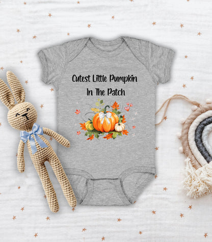 Heather infant bodysuit featuring the phrase "Cutest Little Pumpkin In The Patch" with an adorable fall-themed design of orange and white pumpkins, autumn leaves, hearts, and a sweet bow. Perfect for baby's first fall or pumpkin patch visit.