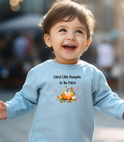 Toddler wearing a light blue long sleeve shirt with 'Cutest Little Pumpkin In The Patch' text and pumpkin graphics.
