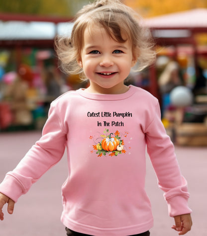 Toddler wearing a pink long sleeve shirt with 'Cutest Little Pumpkin In The Patch' text and pumpkin graphics.