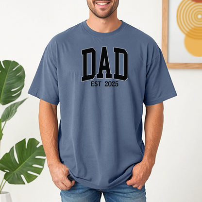 Personalized DAD Est [Year] T-shirt featuring bold varsity-style block lettering with a customizable establishment year. Printed on a soft, relaxed-fit unisex tee in blue jean, this design is perfect for celebrating new or seasoned fathers. Ideal for Father’s Day, birthdays, or family milestones, offering both comfort and a proud personal touch.