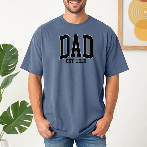 Personalized DAD Est [Year] T-shirt featuring bold varsity-style block lettering with a customizable establishment year. Printed on a soft, relaxed-fit unisex tee in blue jean, this design is perfect for celebrating new or seasoned fathers. Ideal for Father’s Day, birthdays, or family milestones, offering both comfort and a proud personal touch.