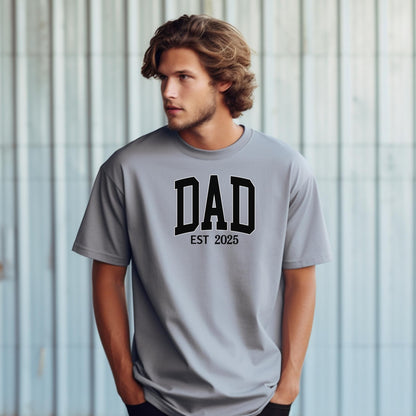 Personalized DAD Est [Year] T-shirt featuring bold varsity-style block lettering with a customizable establishment year. Printed on a soft, relaxed-fit unisex tee in granite, this design is perfect for celebrating new or seasoned fathers. Ideal for Father’s Day, birthdays, or family milestones, offering both comfort and a proud personal touch.