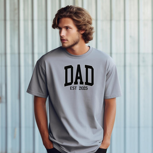 Personalized DAD Est [Year] T-shirt featuring bold varsity-style block lettering with a customizable establishment year. Printed on a soft, relaxed-fit unisex tee in granite, this design is perfect for celebrating new or seasoned fathers. Ideal for Father’s Day, birthdays, or family milestones, offering both comfort and a proud personal touch.