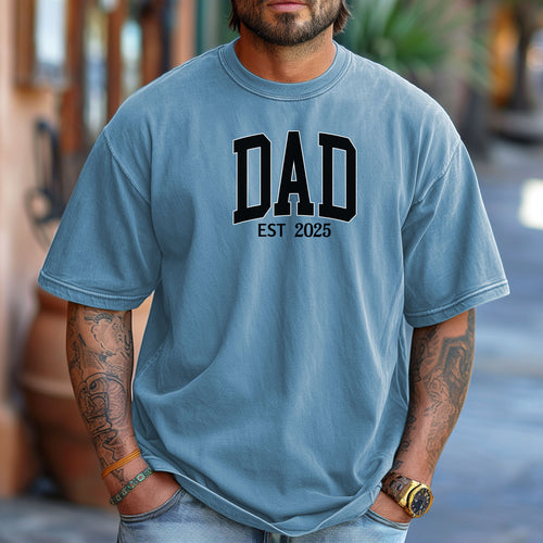 Personalized DAD Est [Year] T-shirt featuring bold varsity-style block lettering with a customizable establishment year. Printed on a soft, relaxed-fit unisex tee in washed denim, this design is perfect for celebrating new or seasoned fathers. Ideal for Father’s Day, birthdays, or family milestones, offering both comfort and a proud personal touch.