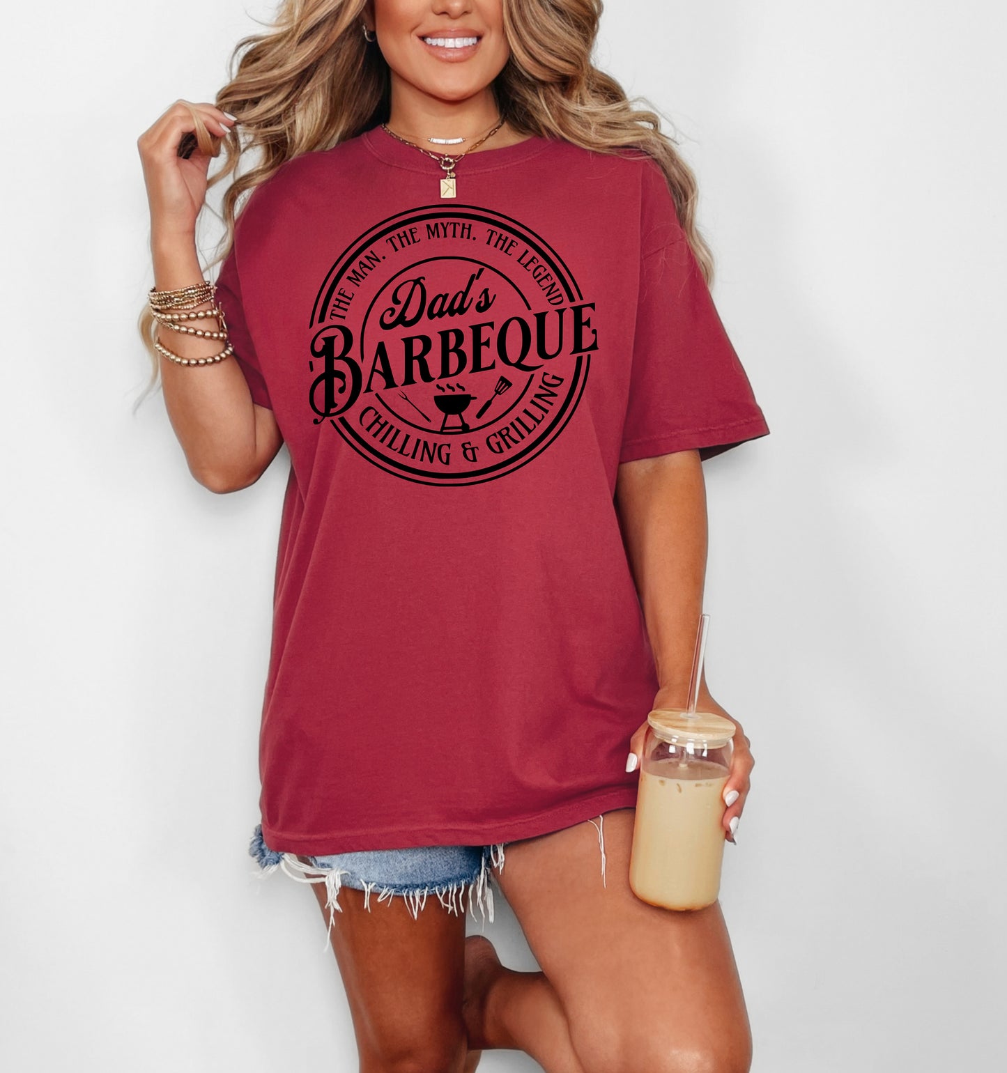 Dad’s Barbeque T-shirt featuring a circular badge-style design with the phrases 'The Man. The Myth. The Legend.' and 'Chilling & Grilling.' The center showcases 'Dad’s Barbeque' in bold lettering with a small grill, fork, and spatula icons. Printed on a chili unisex tee, this shirt is perfect for BBQ-loving dads and makes a fun Father’s Day or birthday gift.