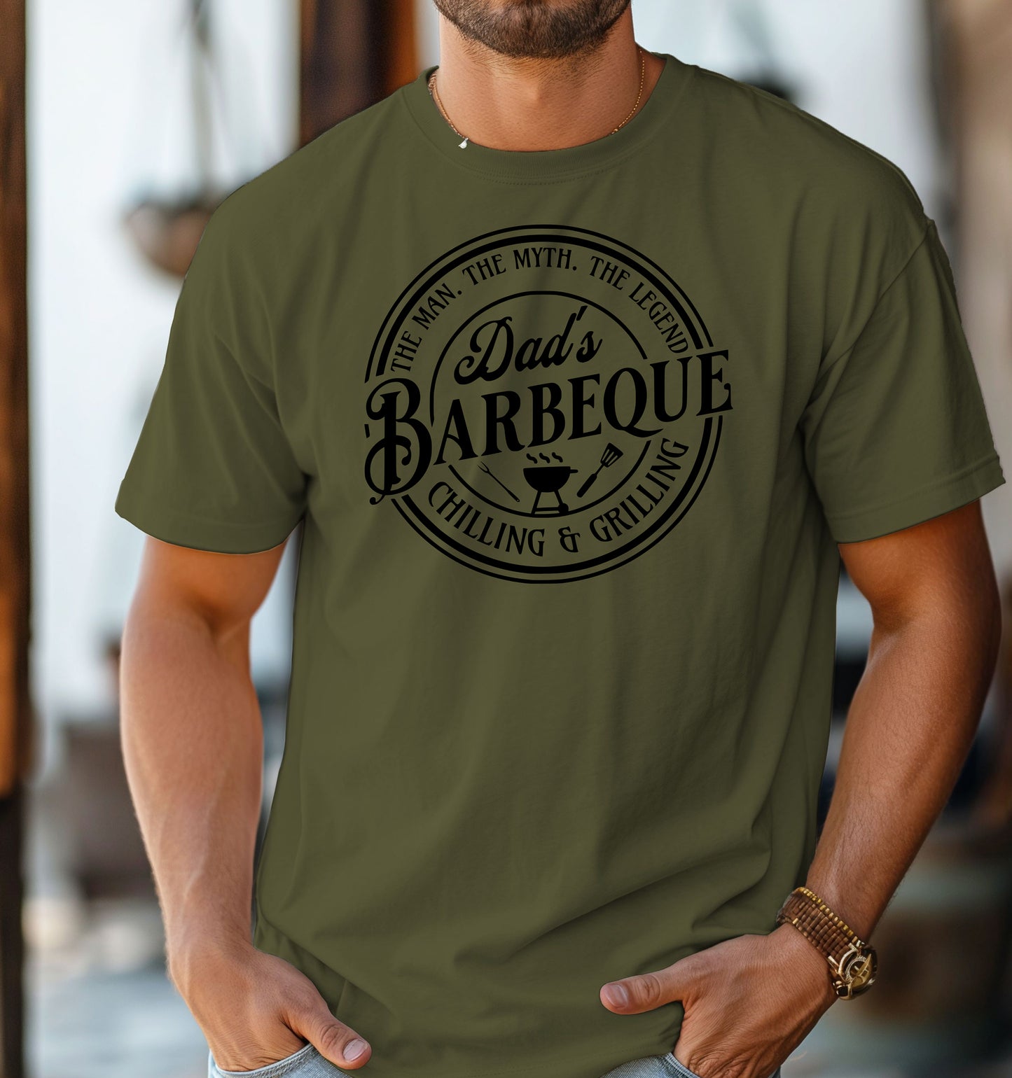 Dad’s Barbeque T-shirt featuring a circular badge-style design with the phrases 'The Man. The Myth. The Legend.' and 'Chilling & Grilling.' The center showcases 'Dad’s Barbeque' in bold lettering with a small grill, fork, and spatula icons. Printed on a hemp color unisex tee, this shirt is perfect for BBQ-loving dads and makes a fun Father’s Day or birthday gift.