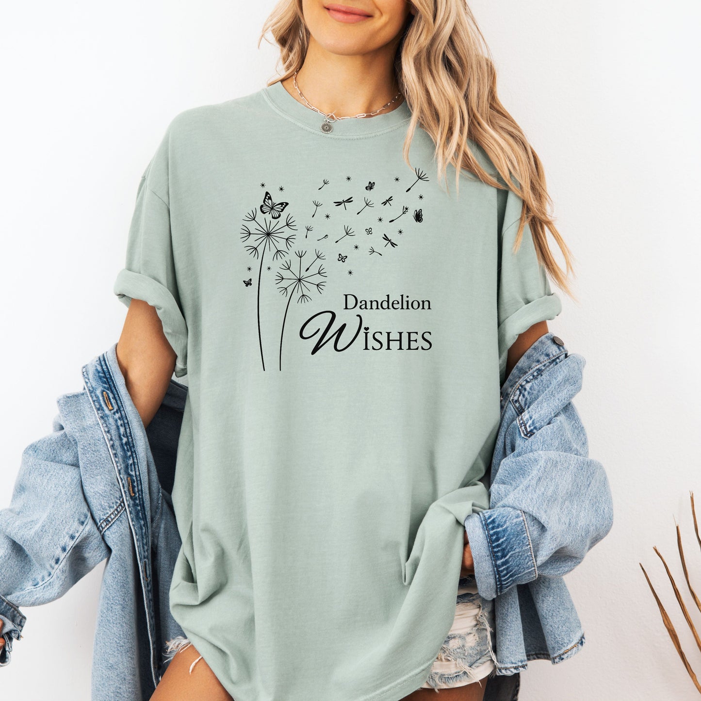 Whimsical dandelions with flying seeds, butterflies, and dragonflies pop in black and white ink against a soft bay (light green) color Comfort Colors tee. Elegant nature motif with clean text that says "Dandelion Wishes".