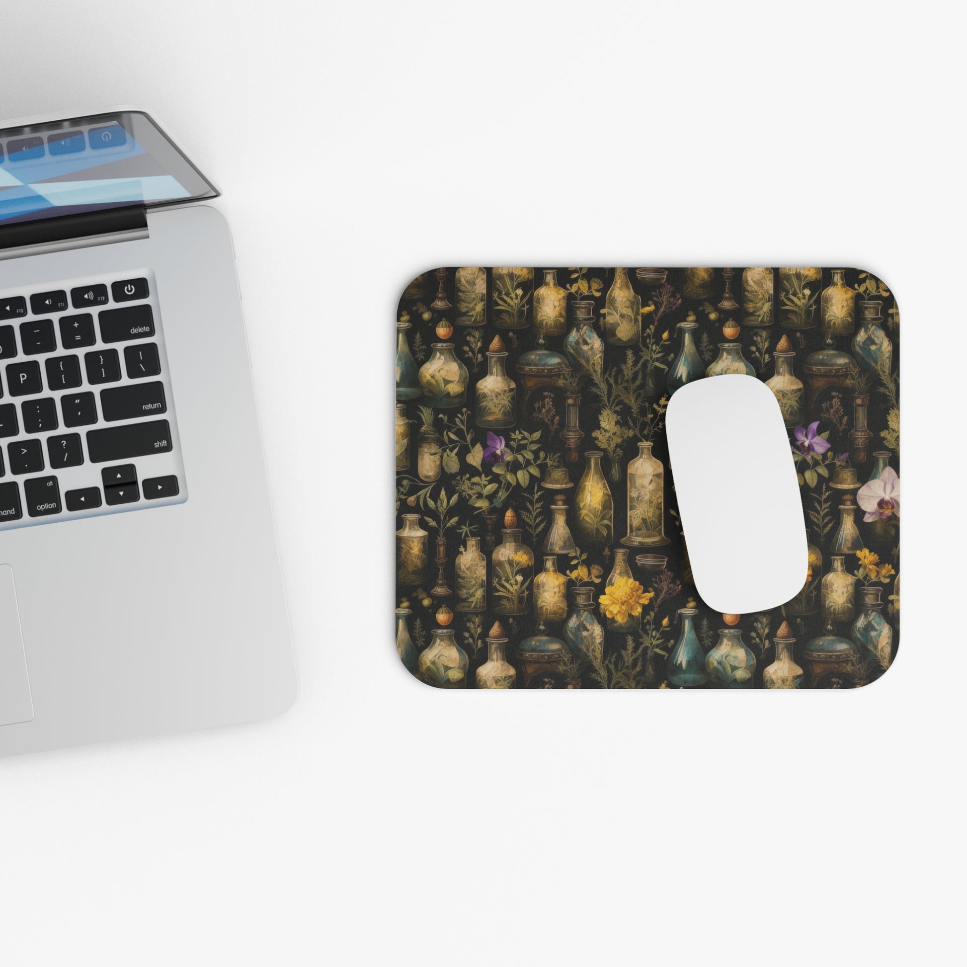 Laptop with a decorative mouse pad featuring apothecary bottles and flowers on a white surface