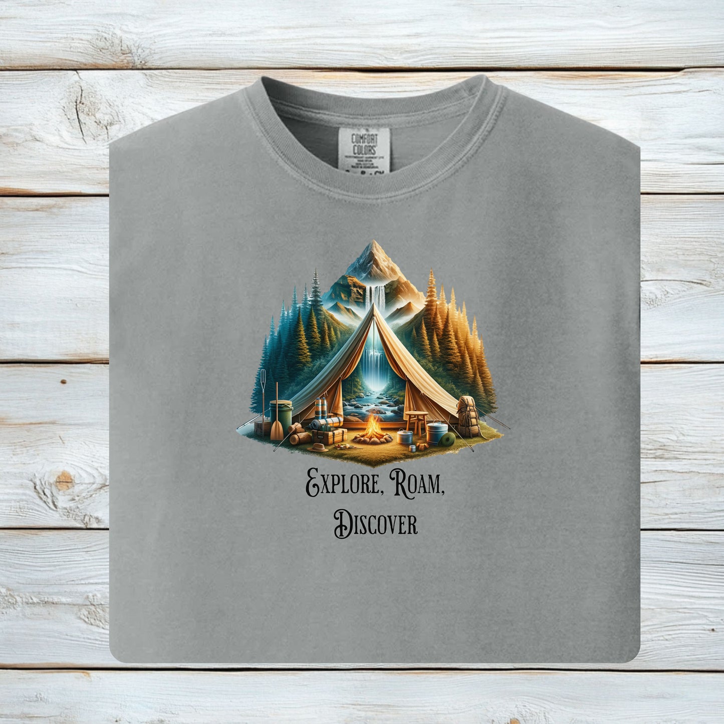Granite “Explore, Roam, Discover” T-shirt featuring a scenic camping design with an open tent framing a mountain, waterfall, pine forest, and river. A cozy campfire, gear, and canoe paddles sit in the foreground, creating an adventurous and tranquil outdoor vibe. Perfect for nature lovers, hikers, and camping enthusiasts seeking wanderlust-inspired apparel.