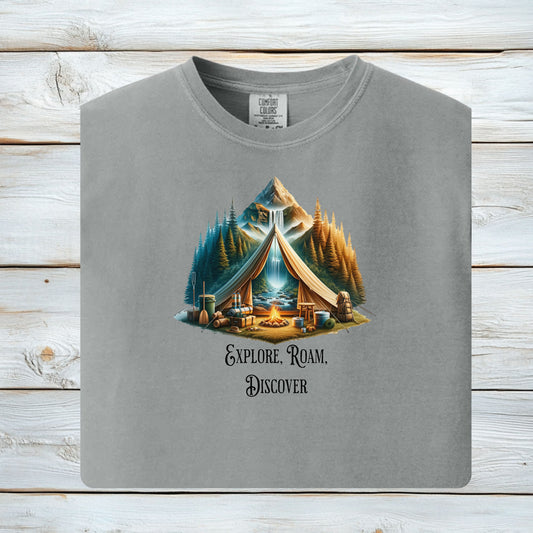 Granite “Explore, Roam, Discover” T-shirt featuring a scenic camping design with an open tent framing a mountain, waterfall, pine forest, and river. A cozy campfire, gear, and canoe paddles sit in the foreground, creating an adventurous and tranquil outdoor vibe. Perfect for nature lovers, hikers, and camping enthusiasts seeking wanderlust-inspired apparel.
