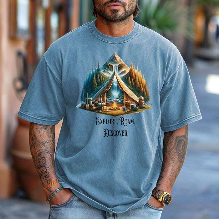 Washed denim “Explore, Roam, Discover” T-shirt featuring a scenic camping design with an open tent framing a mountain, waterfall, pine forest, and river. A cozy campfire, gear, and canoe paddles sit in the foreground, creating an adventurous and tranquil outdoor vibe. Perfect for nature lovers, hikers, and camping enthusiasts seeking wanderlust-inspired apparel.