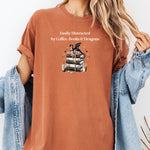 Yam t-shirt featuring the phrase “Easily Distracted by Coffee, Books & Dragons” white text above a whimsical design of a black dragon perched on a stack of ornate books, surrounded by gold hearts and iced coffee cups. A fun and magical design perfect for fantasy lovers who adore caffeine and getting lost in a good book.