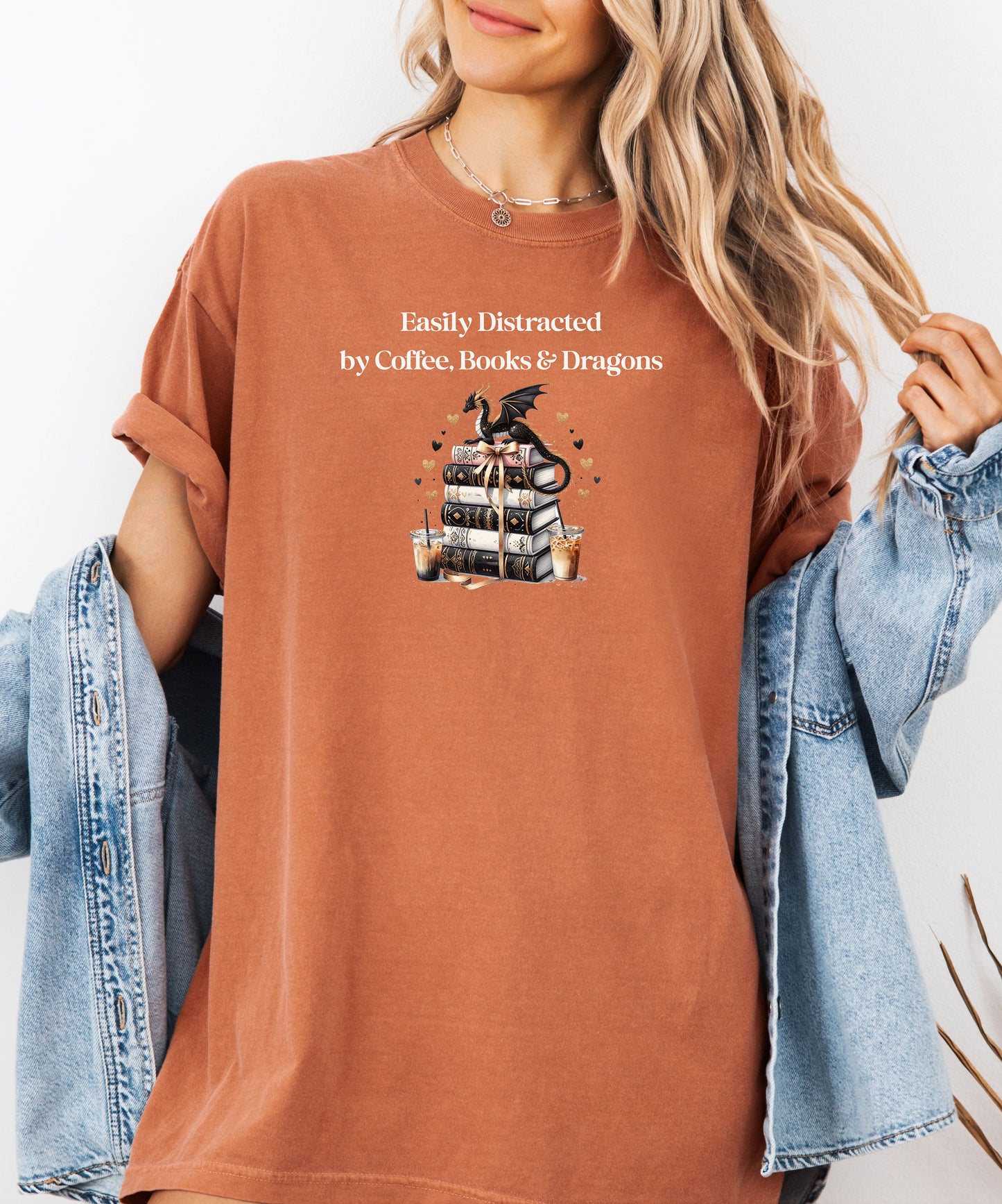 Yam t-shirt featuring the phrase “Easily Distracted by Coffee, Books & Dragons” white text above a whimsical design of a black dragon perched on a stack of ornate books, surrounded by gold hearts and iced coffee cups. A fun and magical design perfect for fantasy lovers who adore caffeine and getting lost in a good book.