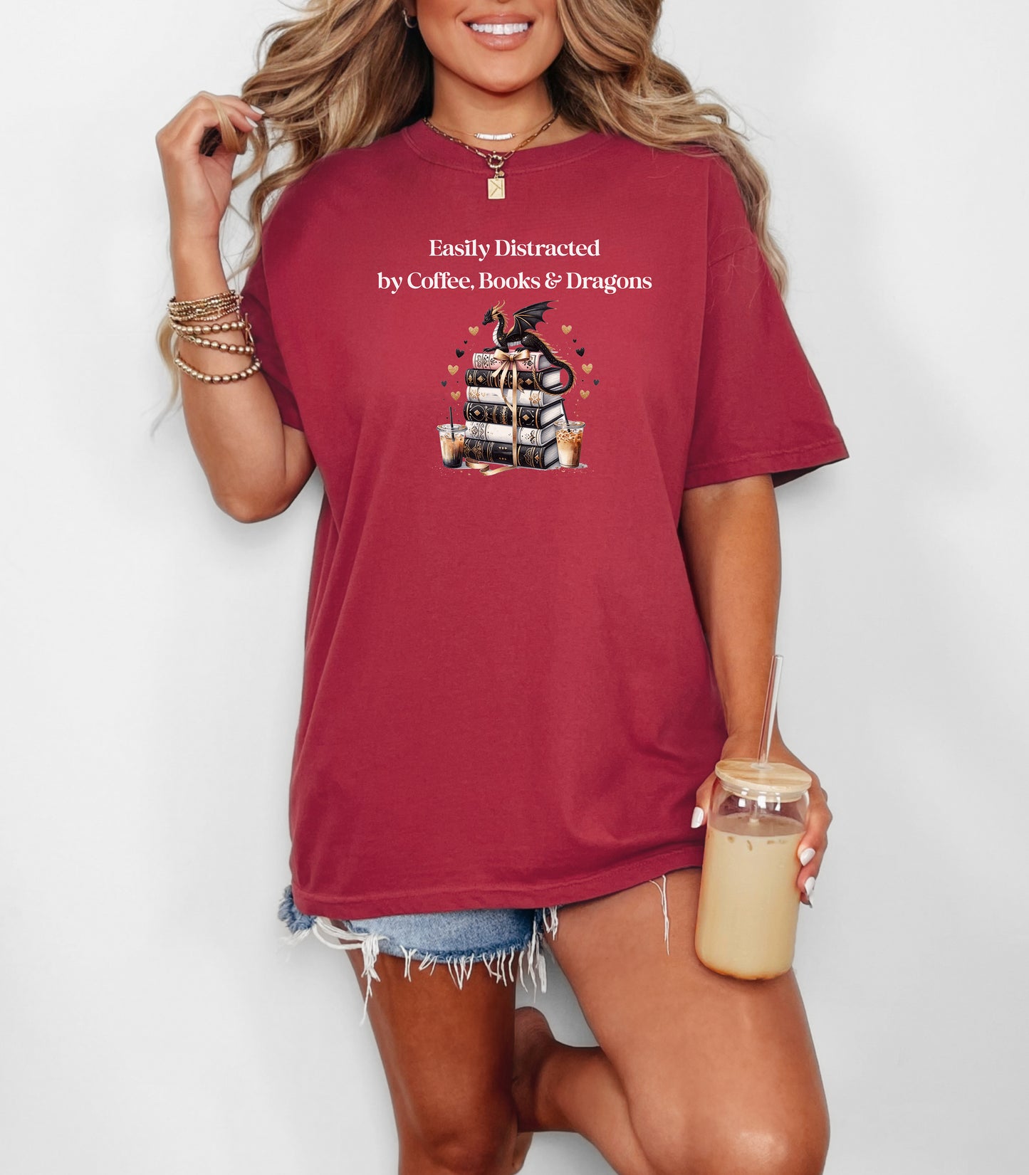 Chili t-shirt featuring the phrase “Easily Distracted by Coffee, Books & Dragons” white text above a whimsical design of a black dragon perched on a stack of ornate books, surrounded by gold hearts and iced coffee cups. A fun and magical design perfect for fantasy lovers who adore caffeine and getting lost in a good book.