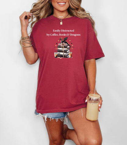 Chili t-shirt featuring the phrase “Easily Distracted by Coffee, Books & Dragons” white text above a whimsical design of a black dragon perched on a stack of ornate books, surrounded by gold hearts and iced coffee cups. A fun and magical design perfect for fantasy lovers who adore caffeine and getting lost in a good book.