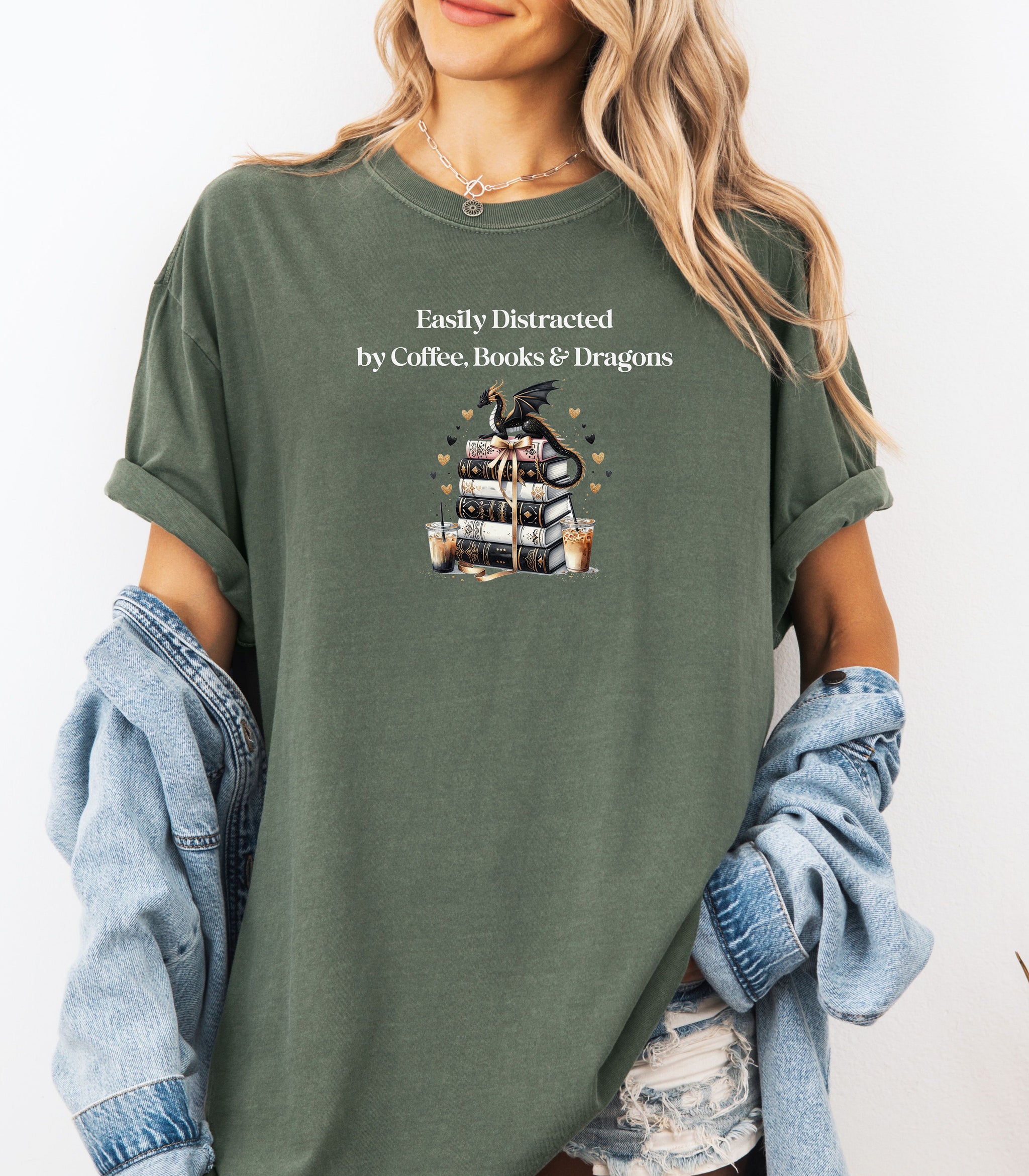 Hemp color t-shirt featuring the phrase “Easily Distracted by Coffee, Books & Dragons” white text above a whimsical design of a black dragon perched on a stack of ornate books, surrounded by gold hearts and iced coffee cups. A fun and magical design perfect for fantasy lovers who adore caffeine and getting lost in a good book.