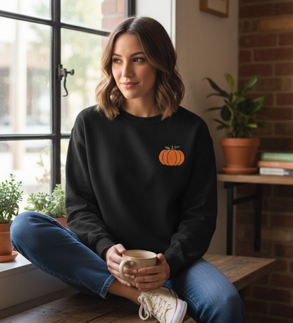 Person wearing a black sweatshirt with an embroidered pumpkin design, holding a coffee cup.