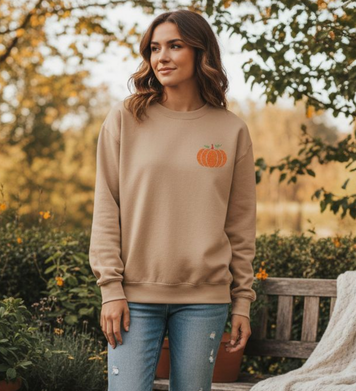 Person wearing a sand sweatshirt with an embroidered pumpkin design, outdoors