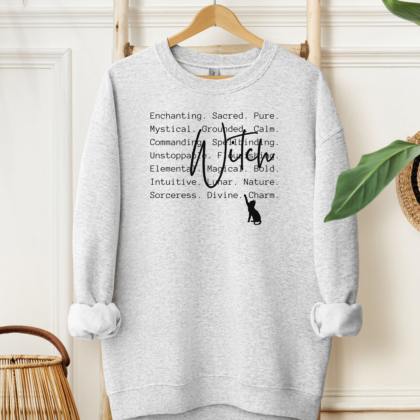 Ash sweatshirt with text and a cat silhouette on a hanger against a white wall.