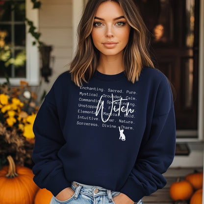 Person wearing a navy blue sweatshirt with Witch text and a cat graphic, standing in front of pumpkins and autumn decorations.