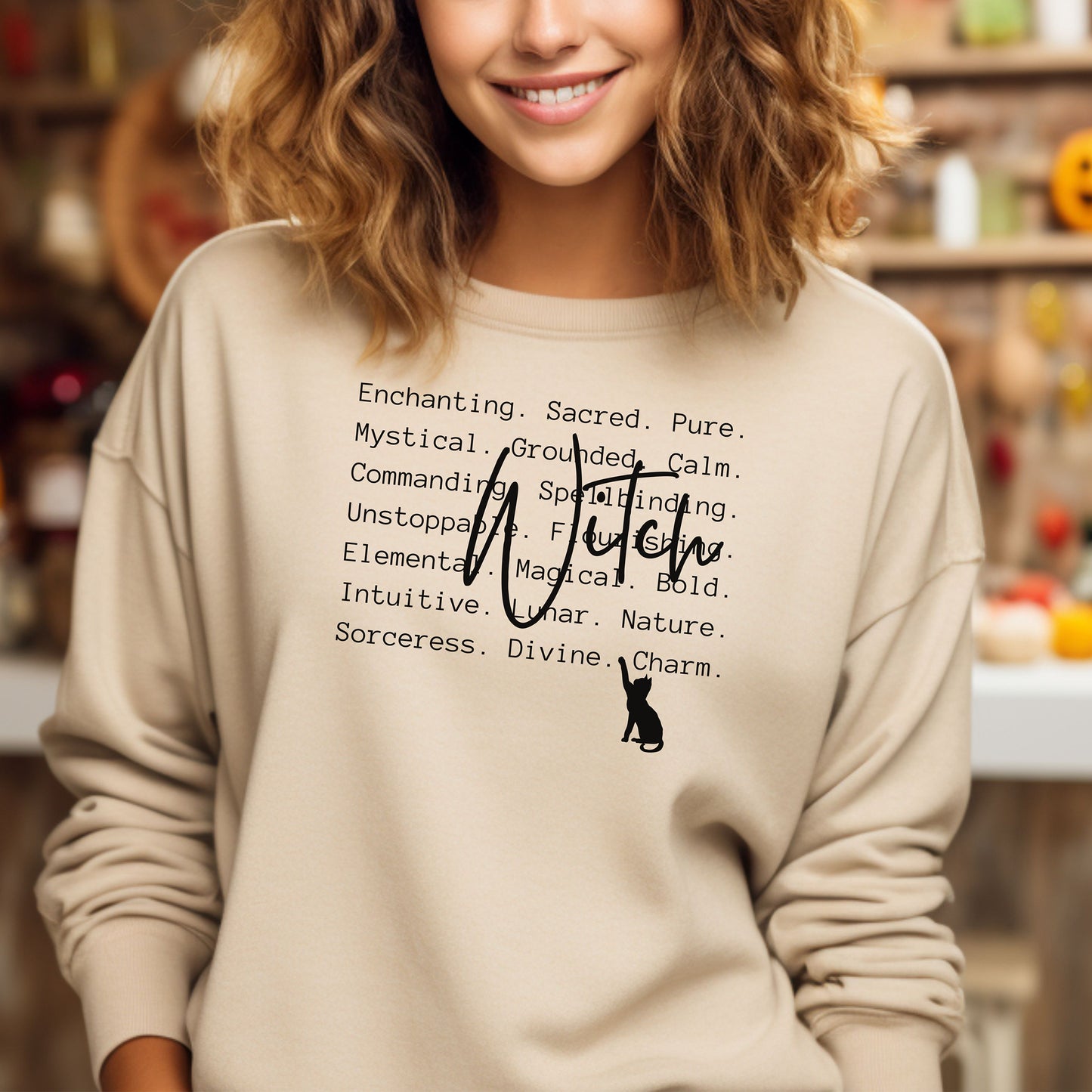 Person wearing a Sanc sweatshirt with Witch text and a black silhouette cat design, standing in front of a fall themed wall.