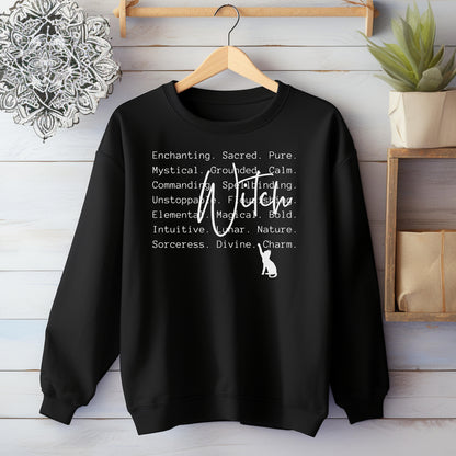 Black sweatshirt with Witch text and a cat graphic on a wooden hanger against a wooden wall.