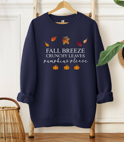 Navy Gildan sweatshirt featuring a festive fall-themed design with colorful autumn leaves, the phrase “Fall Breeze, Crunchy Leaves, Pumpkins Please” in mixed fonts, and four orange pumpkin icons along the bottom. A cozy and stylish piece perfect for embracing crisp air, seasonal vibes, and pumpkin spice everything.