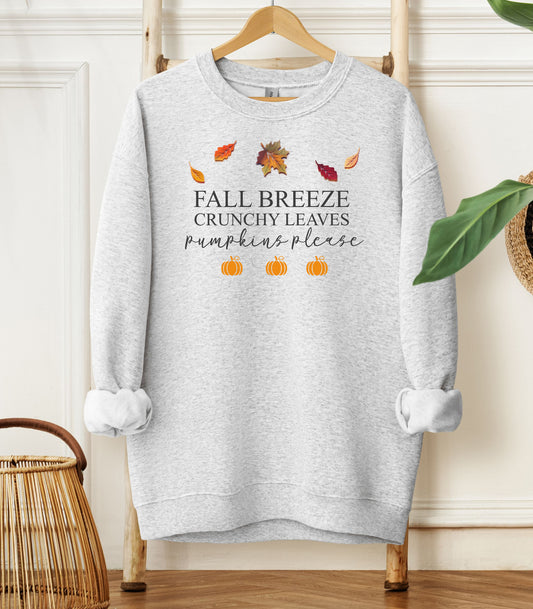 Ash Gildan sweatshirt featuring a festive fall-themed design with colorful autumn leaves, the phrase “Fall Breeze, Crunchy Leaves, Pumpkins Please” in mixed fonts, and four orange pumpkin icons along the bottom. A cozy and stylish piece perfect for embracing crisp air, seasonal vibes, and pumpkin spice everything.