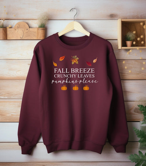 Maroon Gildan sweatshirt featuring a festive fall-themed design with colorful autumn leaves, the phrase “Fall Breeze, Crunchy Leaves, Pumpkins Please” in mixed fonts, and four orange pumpkin icons along the bottom. A cozy and stylish piece perfect for embracing crisp air, seasonal vibes, and pumpkin spice everything.